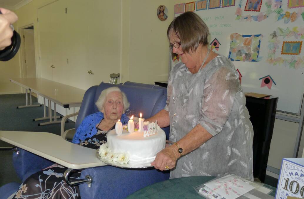 Mrs. Hazel Browne blowing out her candles on her cake held by Mrs. Marilyn Nicholl.