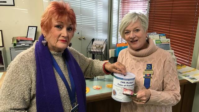 Pamela Matheson and Diana Anderson contributing unused foreign currency to the CWA Coins of Friendship collection tin at the Mudgee Guardian office.