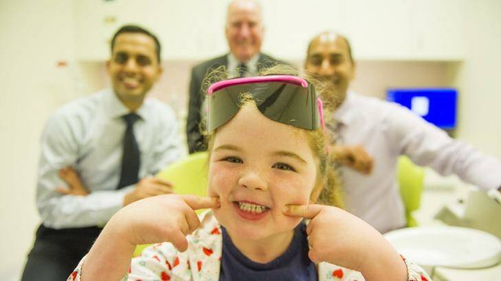 Arabella Ferguson, 5, is happy to be sitting in the dental clinic chair with dentists (left) Dr Sanjiv Pathak and (right) Dr Atul Manani.  Photo: Jay Cronan