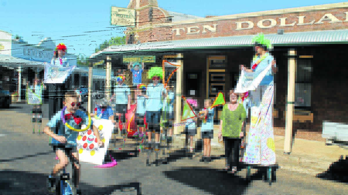 Carol Swadling of the Ten Dollar Town Motel has a visit from Gulgong Public School’s Ten Dollar Circus, waving Ten Dollar tea-towels available for ten dollars at the Gulgong Pioneers Museum.