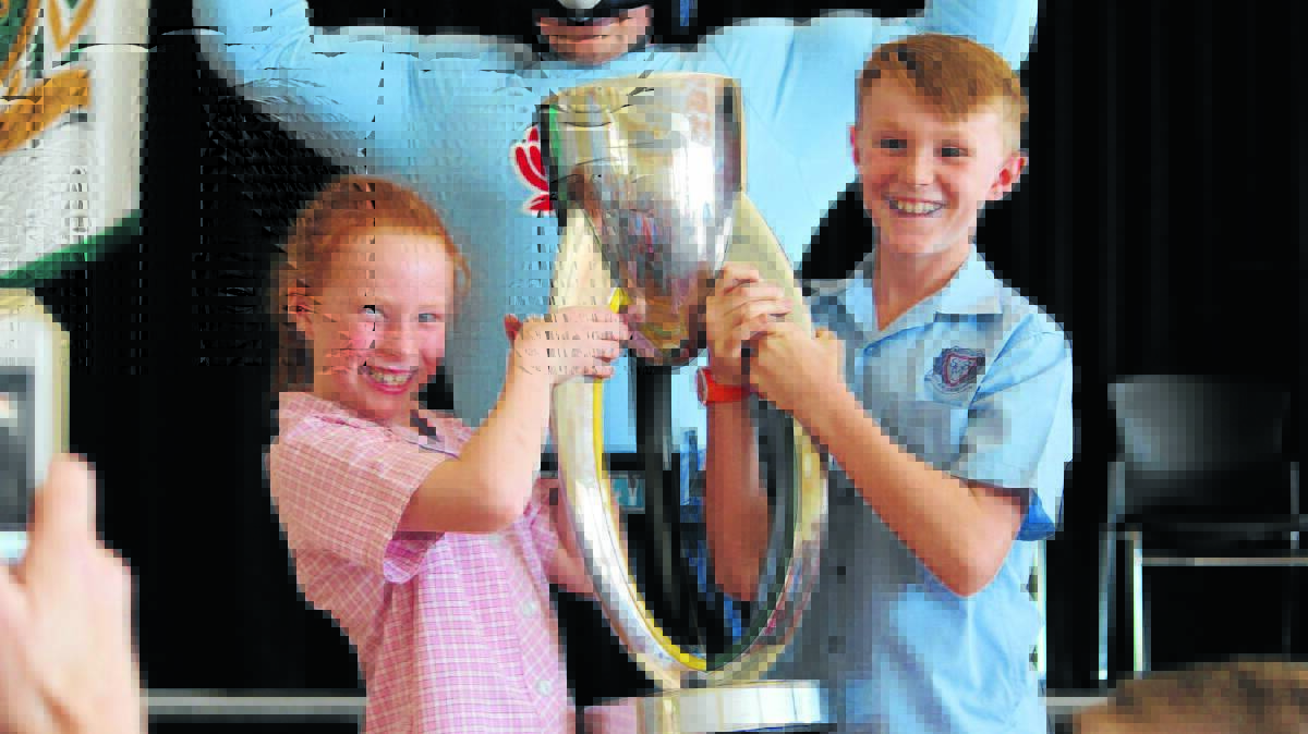 St Matthews Catholic School students Eliza and Flynn English lift the Super Rugby trophy with NSW Waratahs mascot Tah Man showing his muscles. Photo courtesy: Eliza Biddle