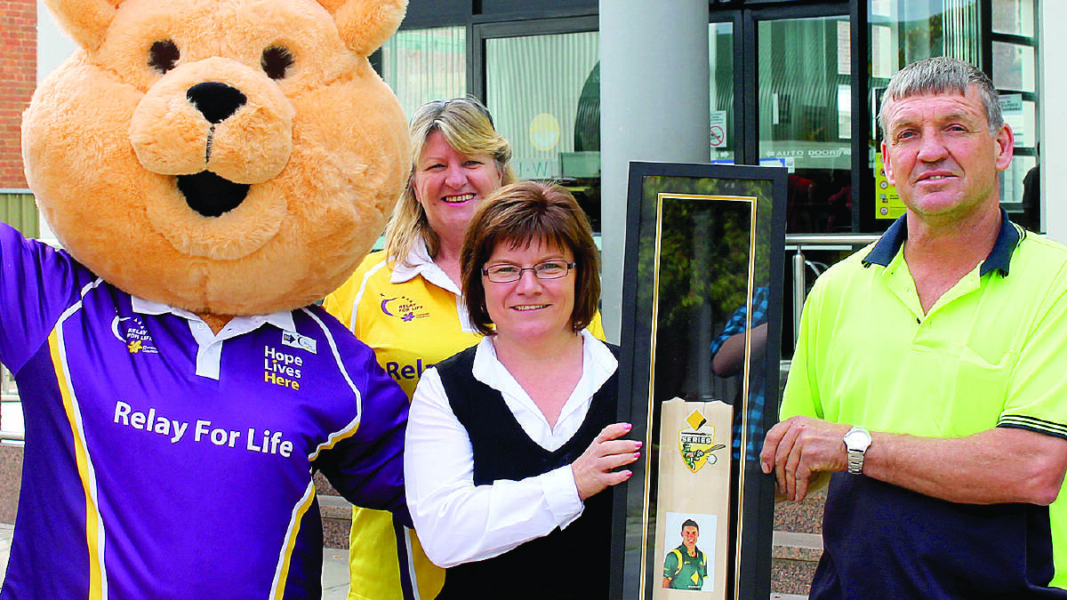 Cancer Council mascot Dougal Bear, Relay For Life committee member Gabrielle Peterson-Condon, and Commonwealth Bank Mudgee Branch Manager Tina Palfreyman present Murray Stanford for cricket bat signed by Australian great Mike Hussey, won in the Relay online auction.