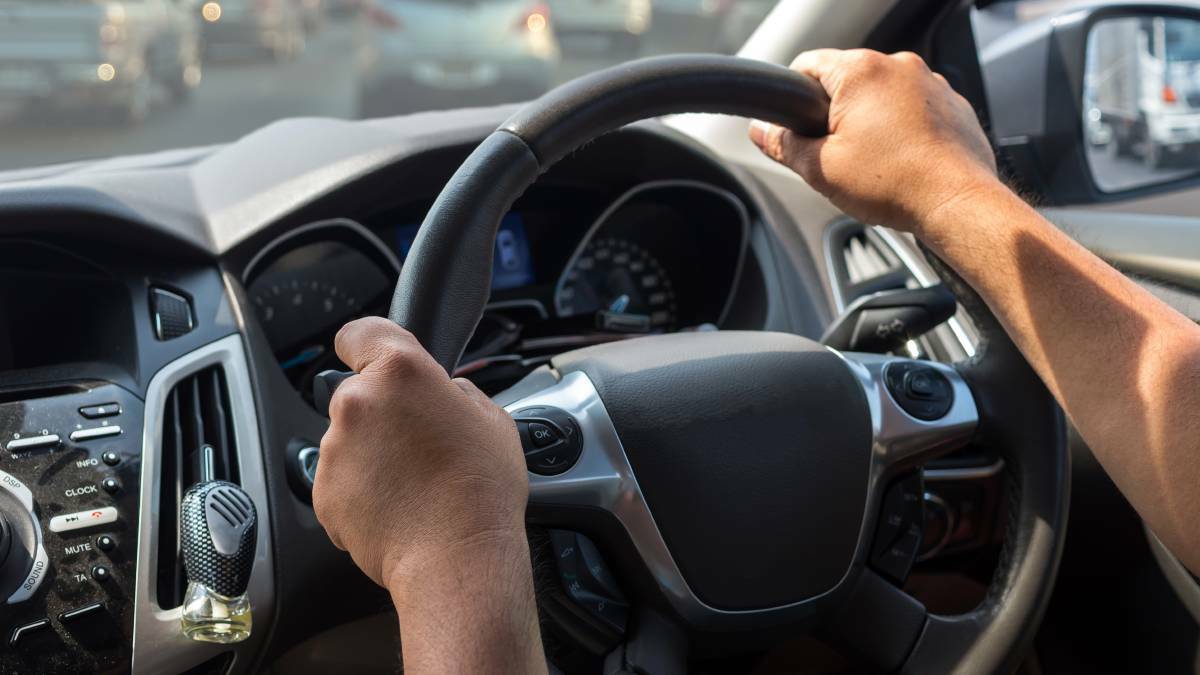 A file image of a person with their hands on a car's steering wheel.
