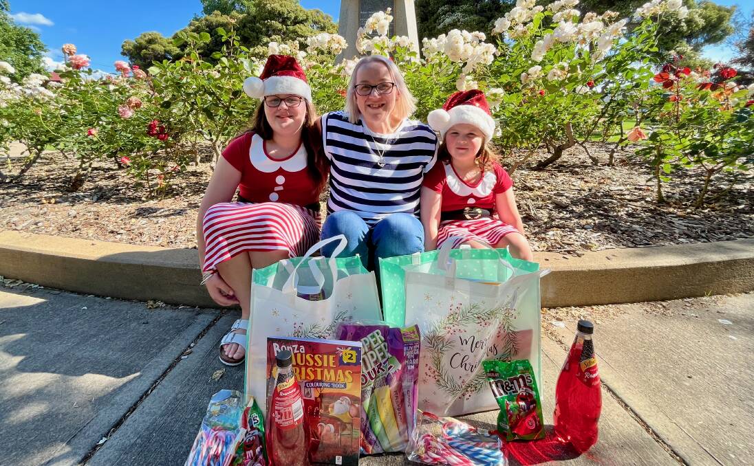MERRY: Amy Lee with her daughters Ruby (left) and Matilda (right) at Robertson Park, Mudgee with a collection of items for their 'reverse advent calendar' hamper. Picture: BENJAMIN PALMER