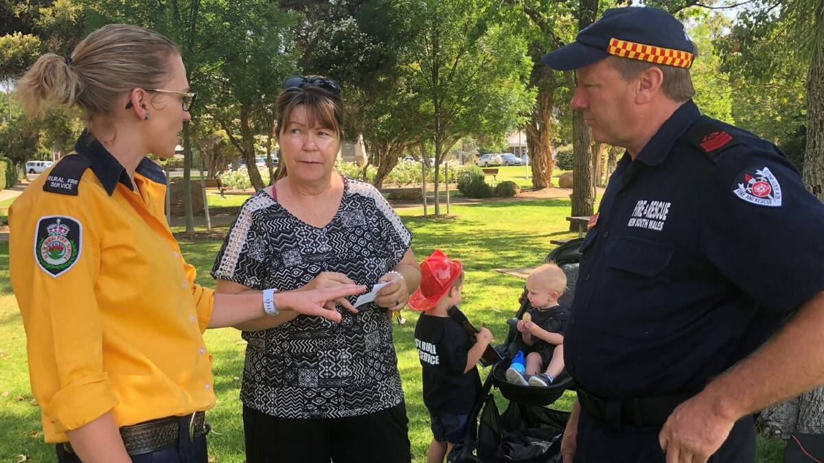 Kennedy Porter (RFS) and Craig Underwood (FRNSW) discuss with Johanna Mitchell of Mudgee how to select the proper fire extinguisher for home use and what other steps she and her family can take to get prepared. Young future fire fighters in the background are Kennedy's sons Jack (red helmet) and Toby. Photo: NSW RFS.