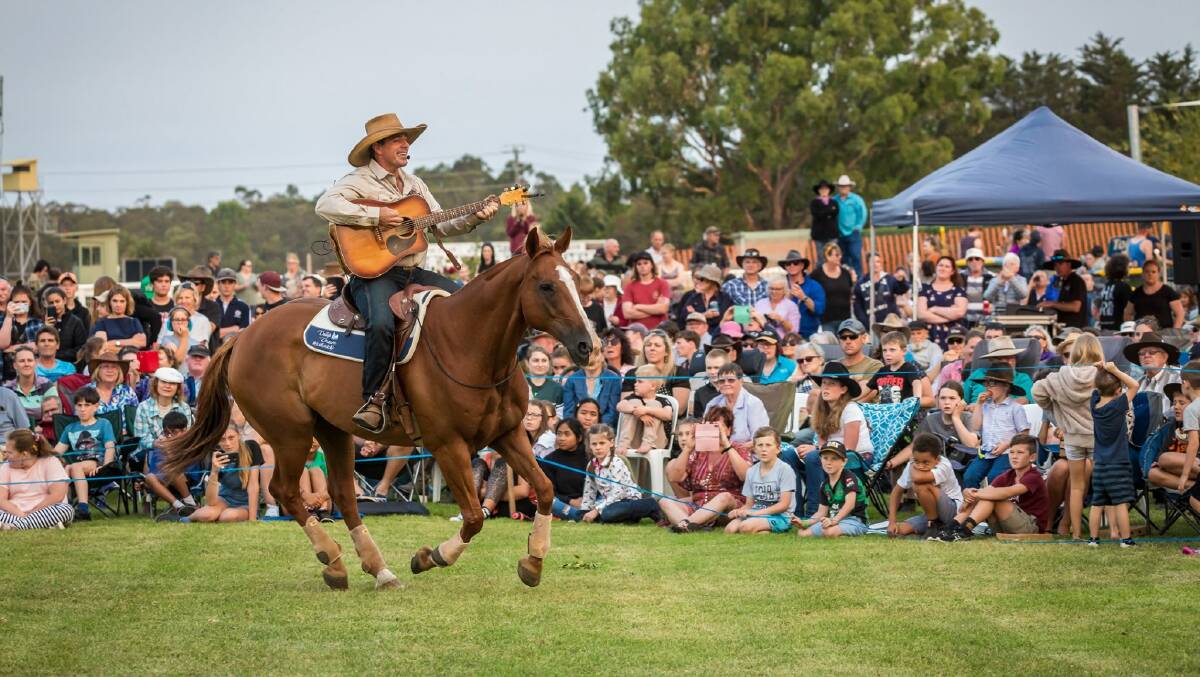 Tom Curtain performing to a large crowd while riding a horse and playing a guitar. Photo: Savvy Social