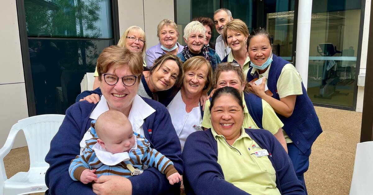Hazel (front left) holding her grandson Thomas with a group of smiling colleagues at her farewell lunch. Photo: Benjamin Palmer